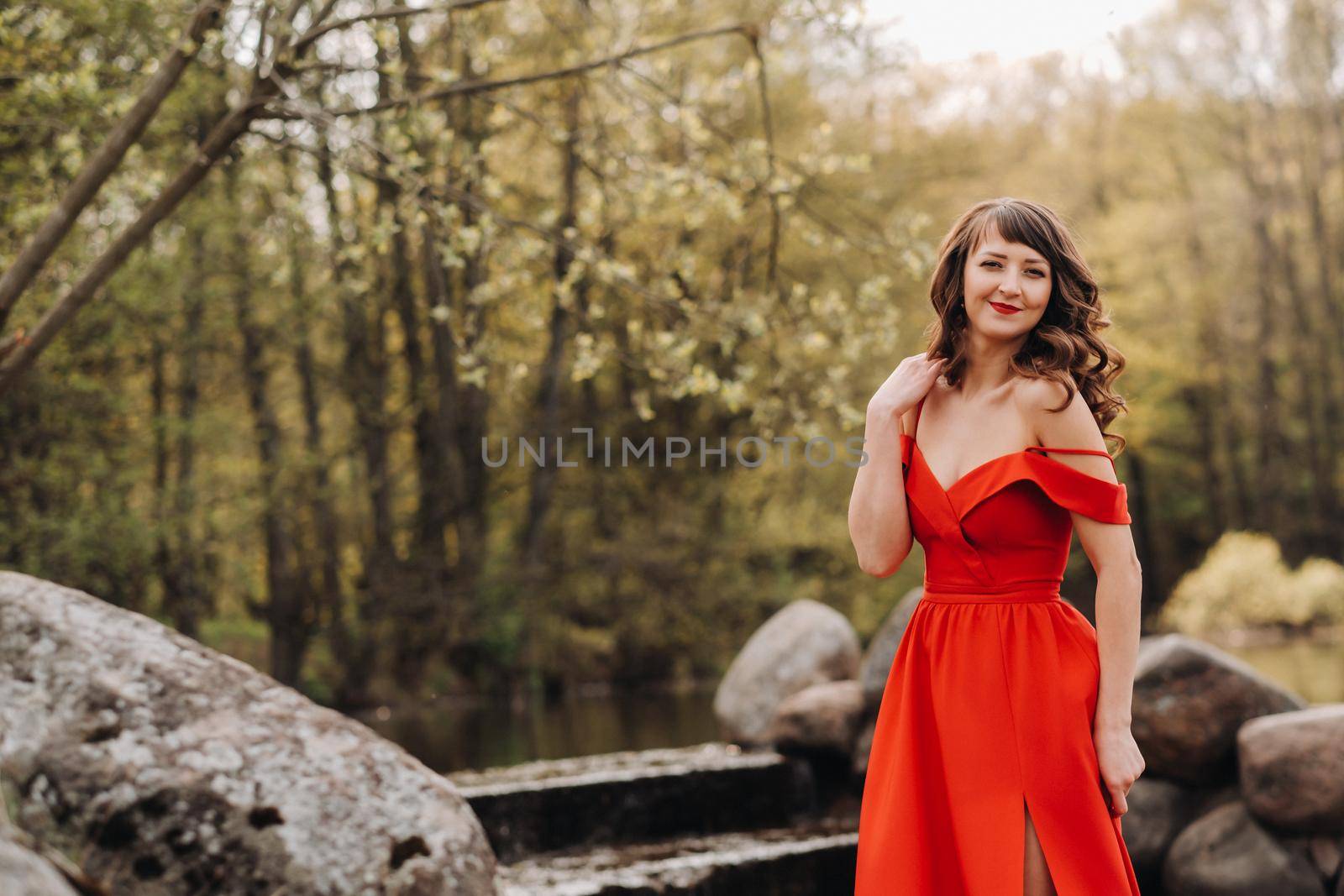 a young beautiful girl with long brown hair , in a long red dress comes down the stairs near the lake