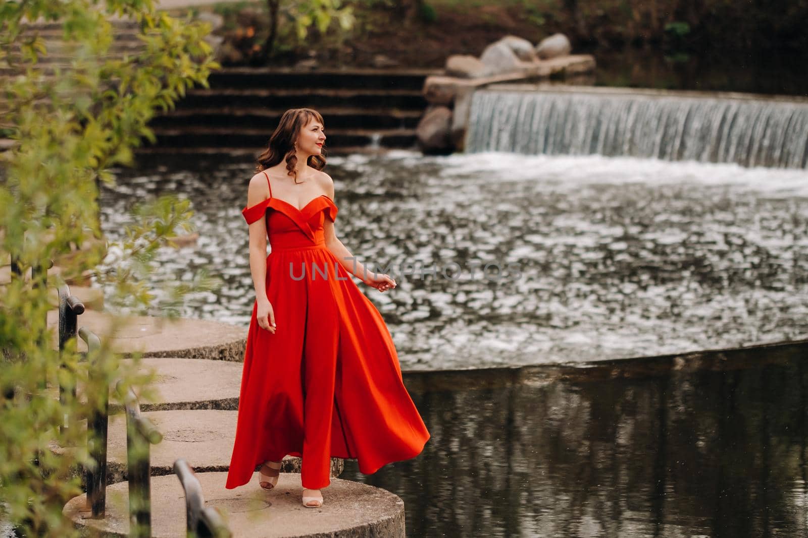 girl in a long red dress near the lake in the Park at sunset