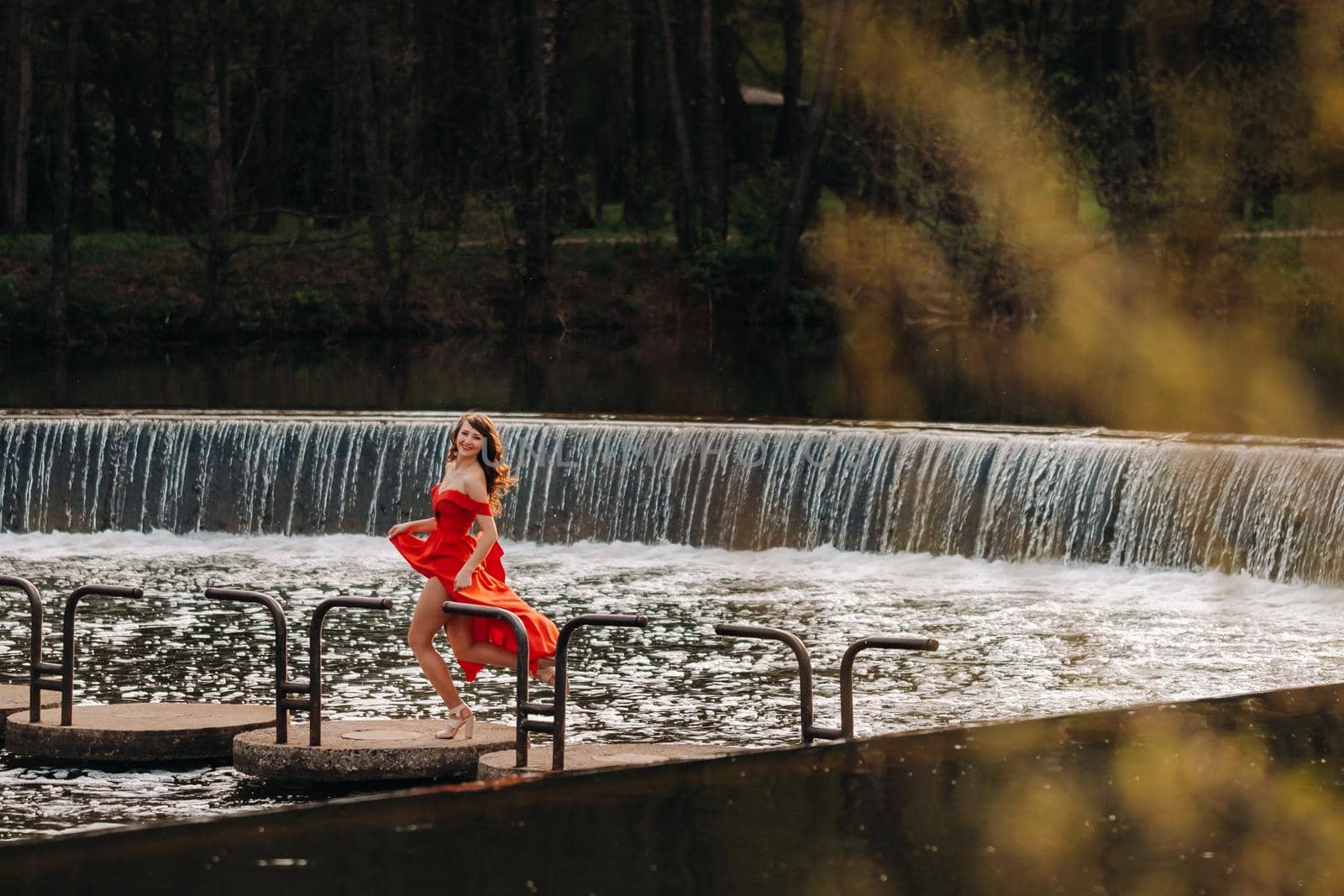 girl in a long red dress near the lake in the Park at sunset. by Lobachad