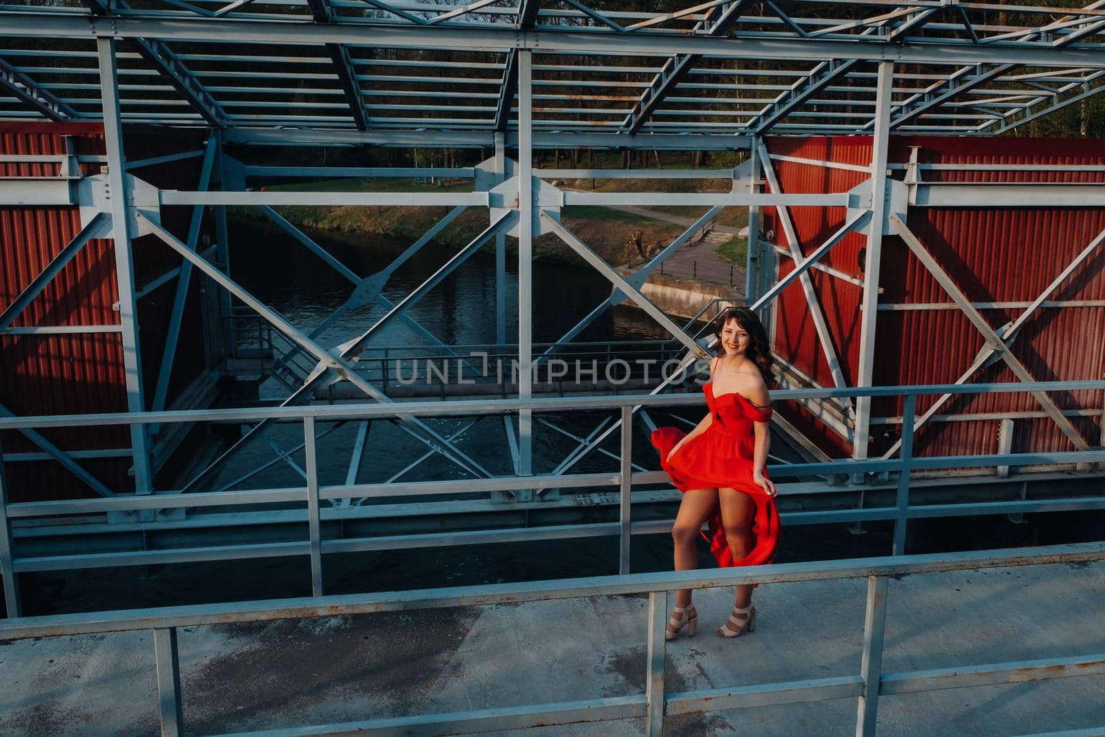 A girl in a red dress on a dam near a river at sunset.