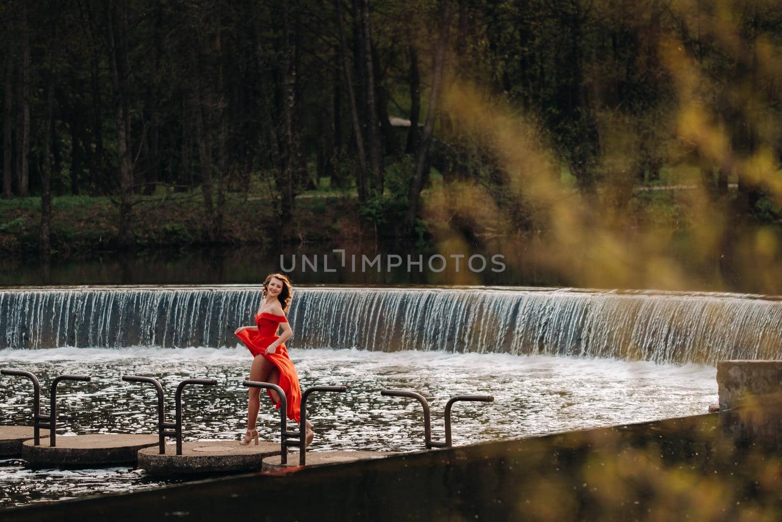 girl in a long red dress near the lake in the Park at sunset. by Lobachad