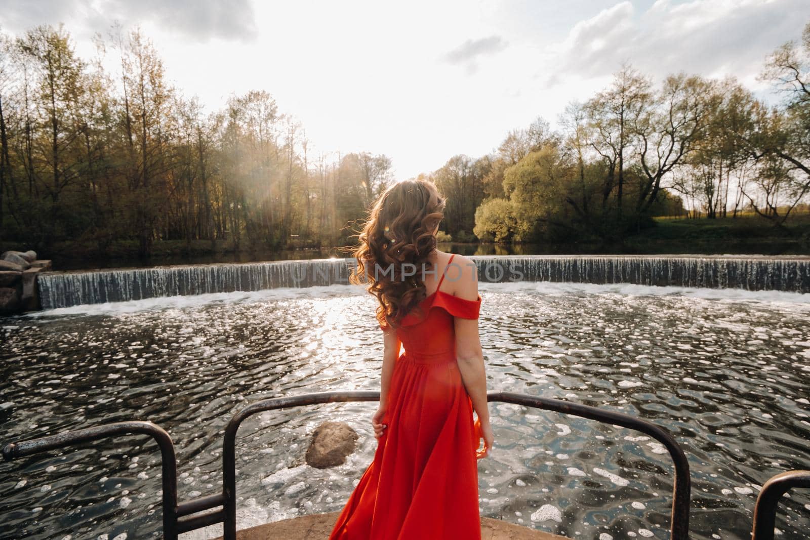 girl in a long red dress near the lake in the Park at sunset