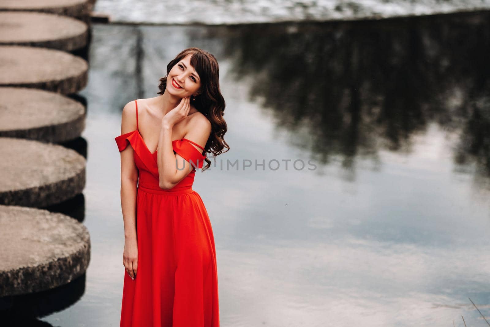 girl in a long red dress near the lake in the Park at sunset