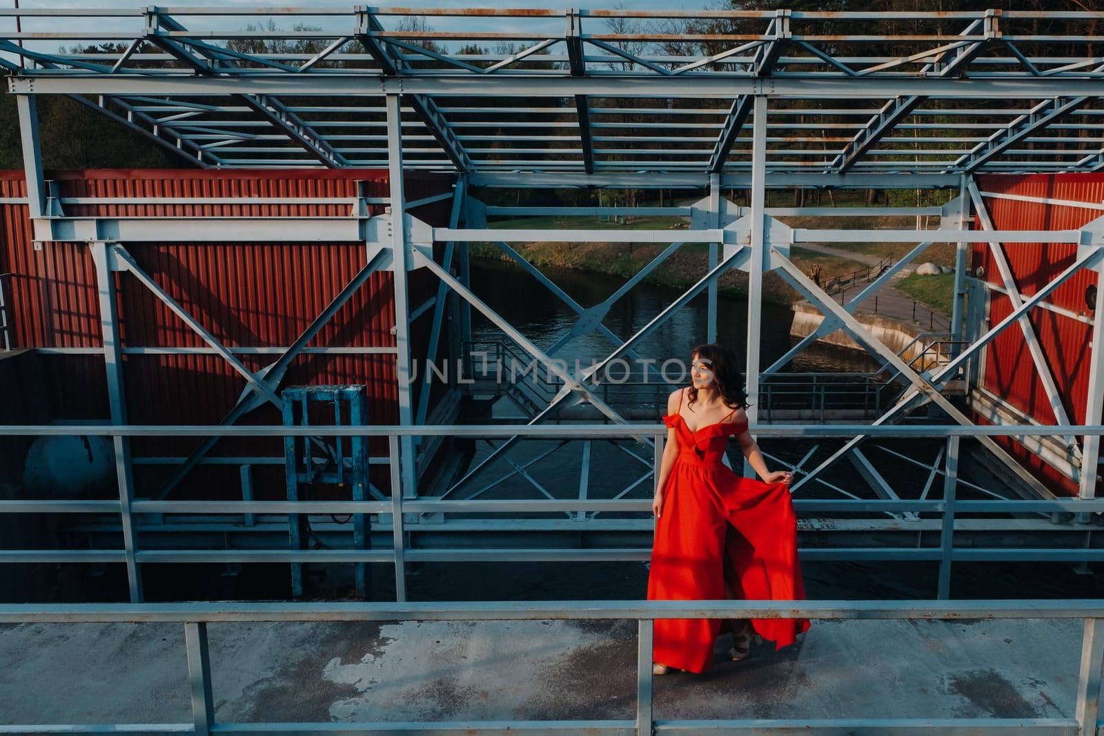 A girl in a red dress on a dam near a river at sunset by Lobachad