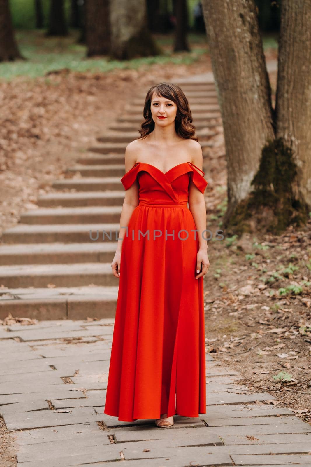 Spring Portrait of a laughing girl in a long red dress with long hair walking in the Park in the woods