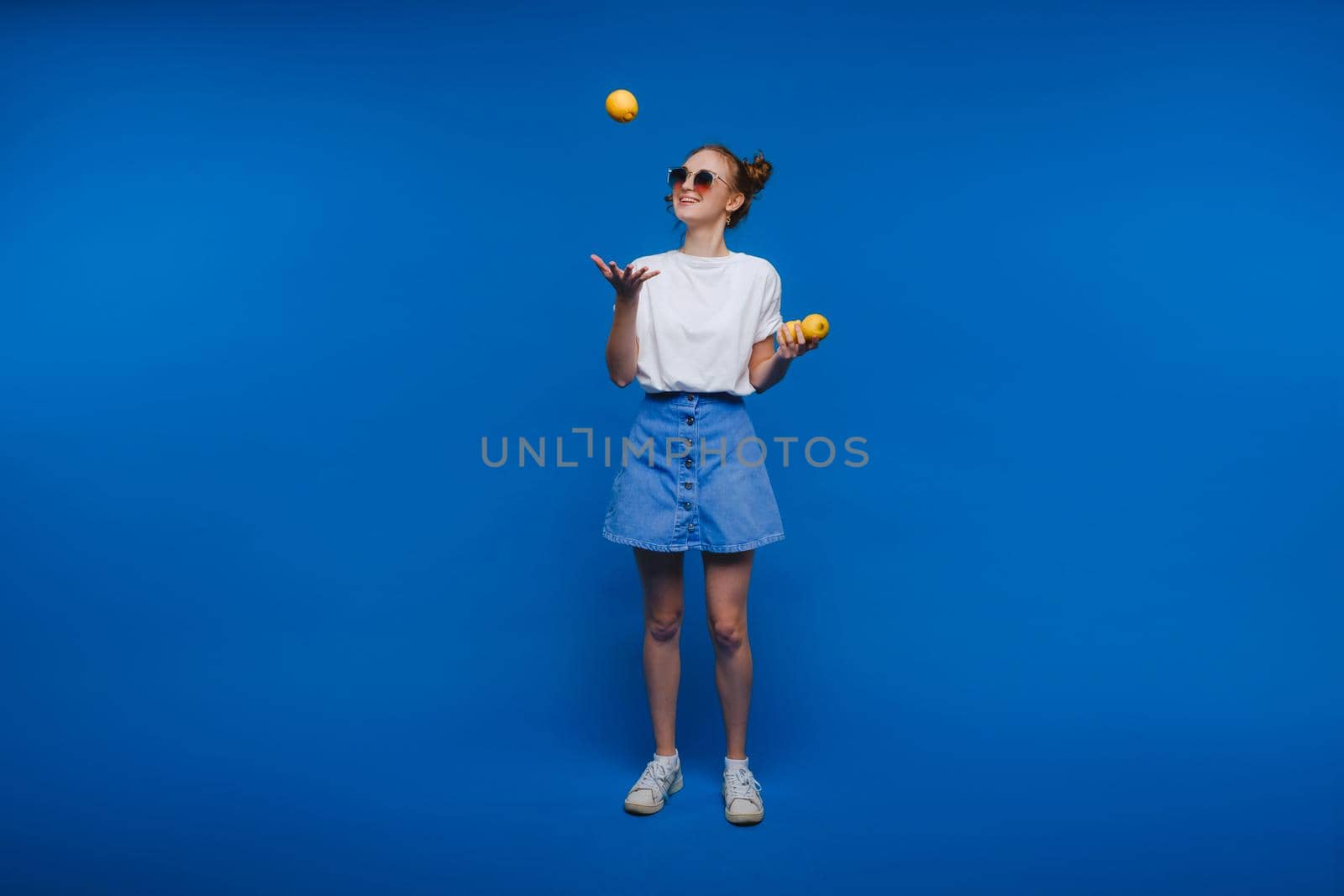 a young beautiful girl standing on a blue background holding lemons in her hand. Smiles.