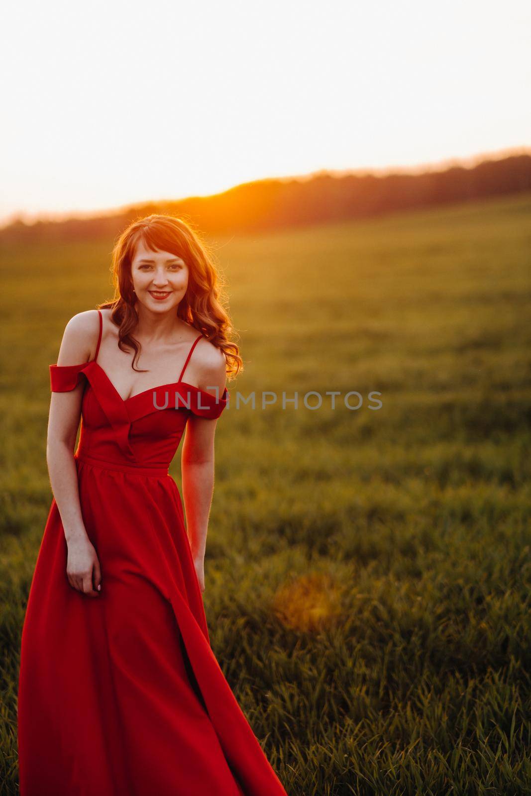 a beautiful girl in spring in a red dress is walking in a field at sunset. Taken from the air by a quadrocopter.