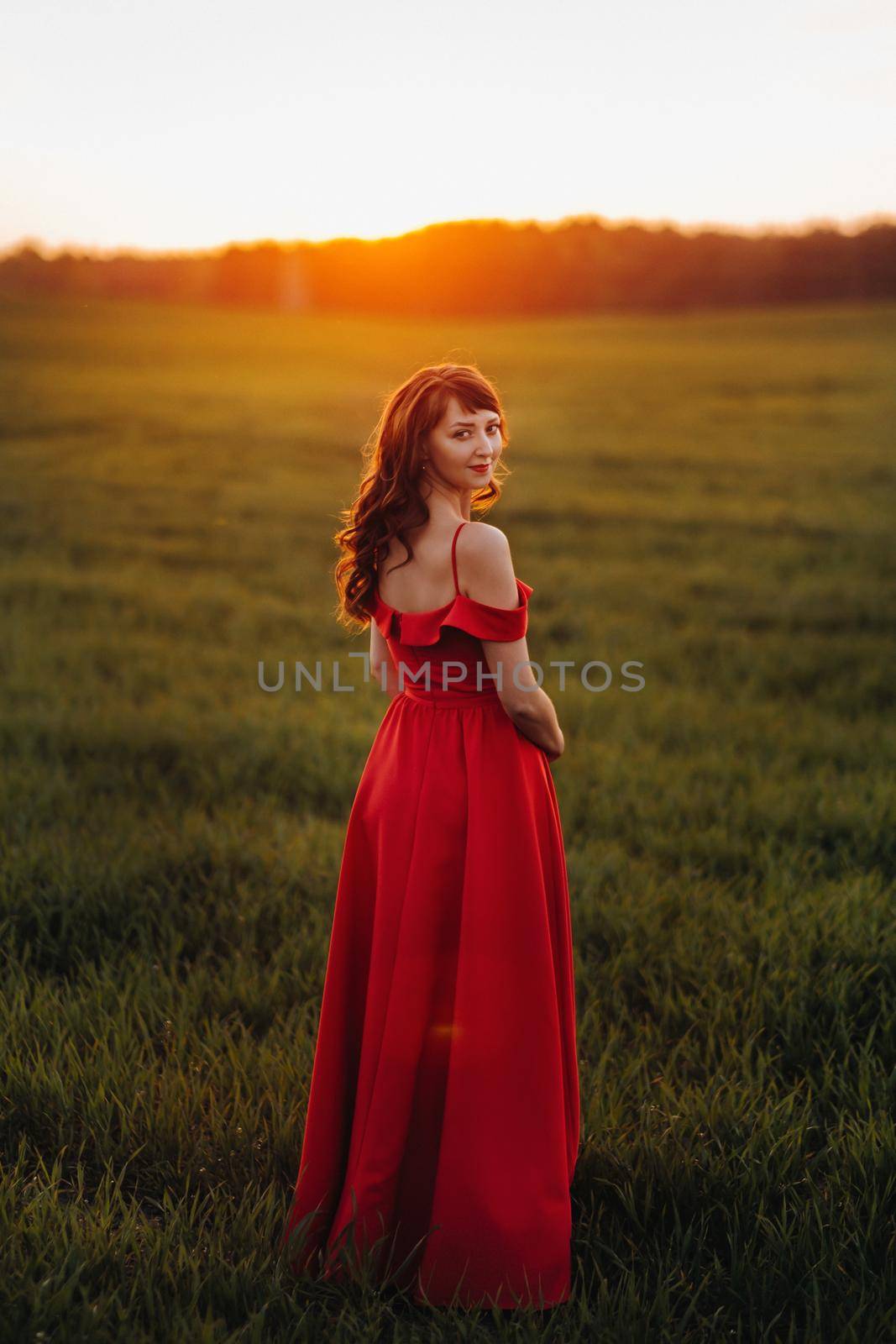 a beautiful girl in spring in a red dress is walking in a field at sunset. Taken from the air by a quadrocopter by Lobachad
