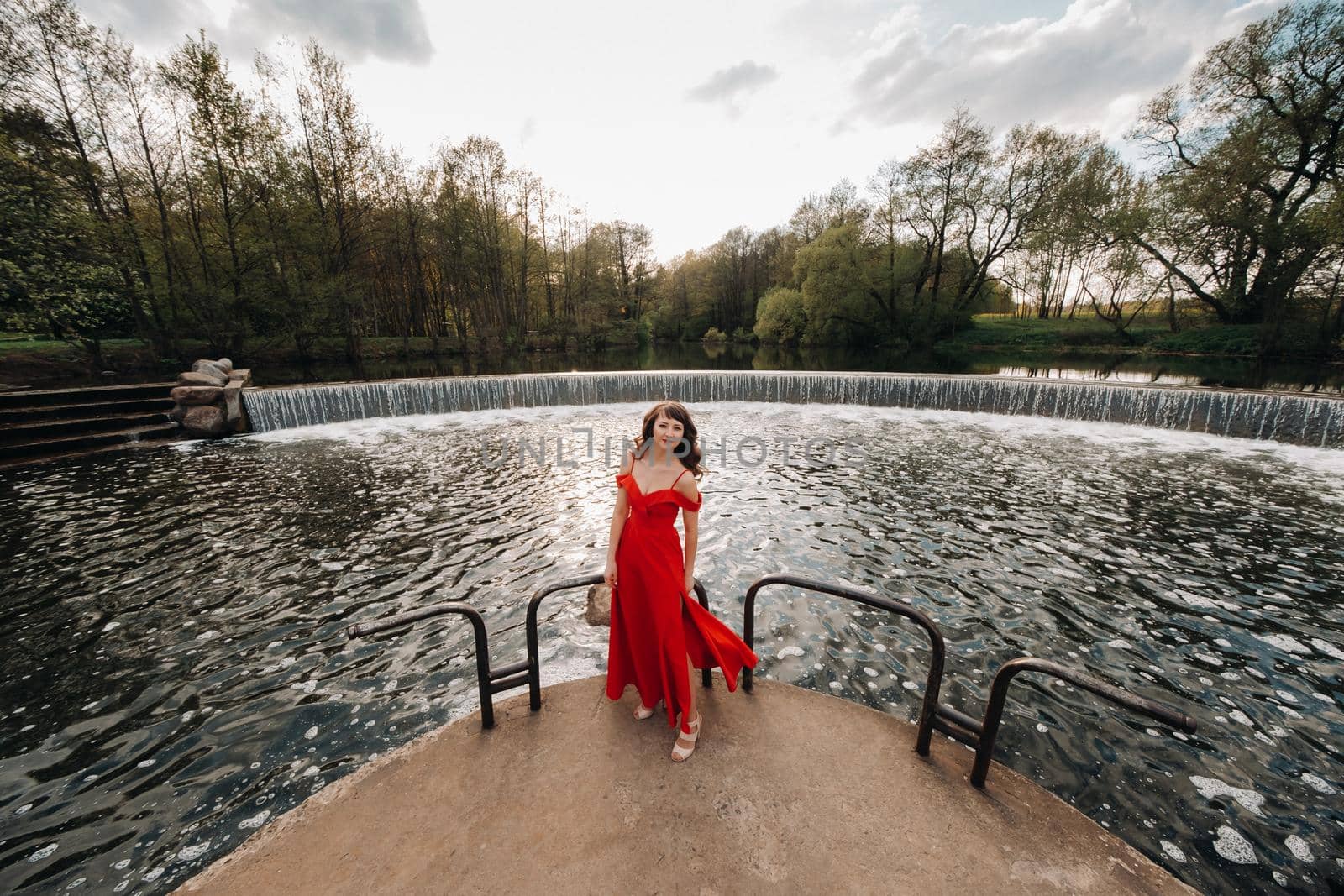 girl in a long red dress near the lake in the Park at sunset