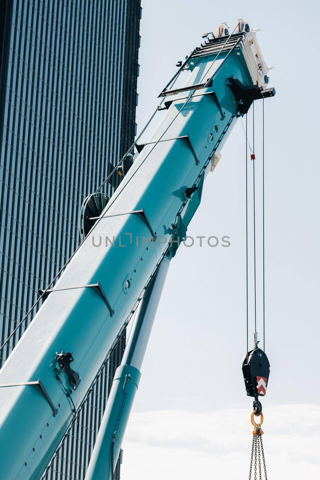 blue crane lifting mechanism with hooks near the glass modern building, crane and hydraulic high lift up to 120 meters.