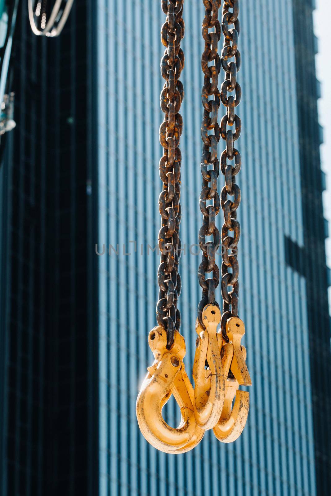 The hooks of the mobile crane near the glass of high buildings.Lots of hooks hanging from chains suspended from a crane by Lobachad