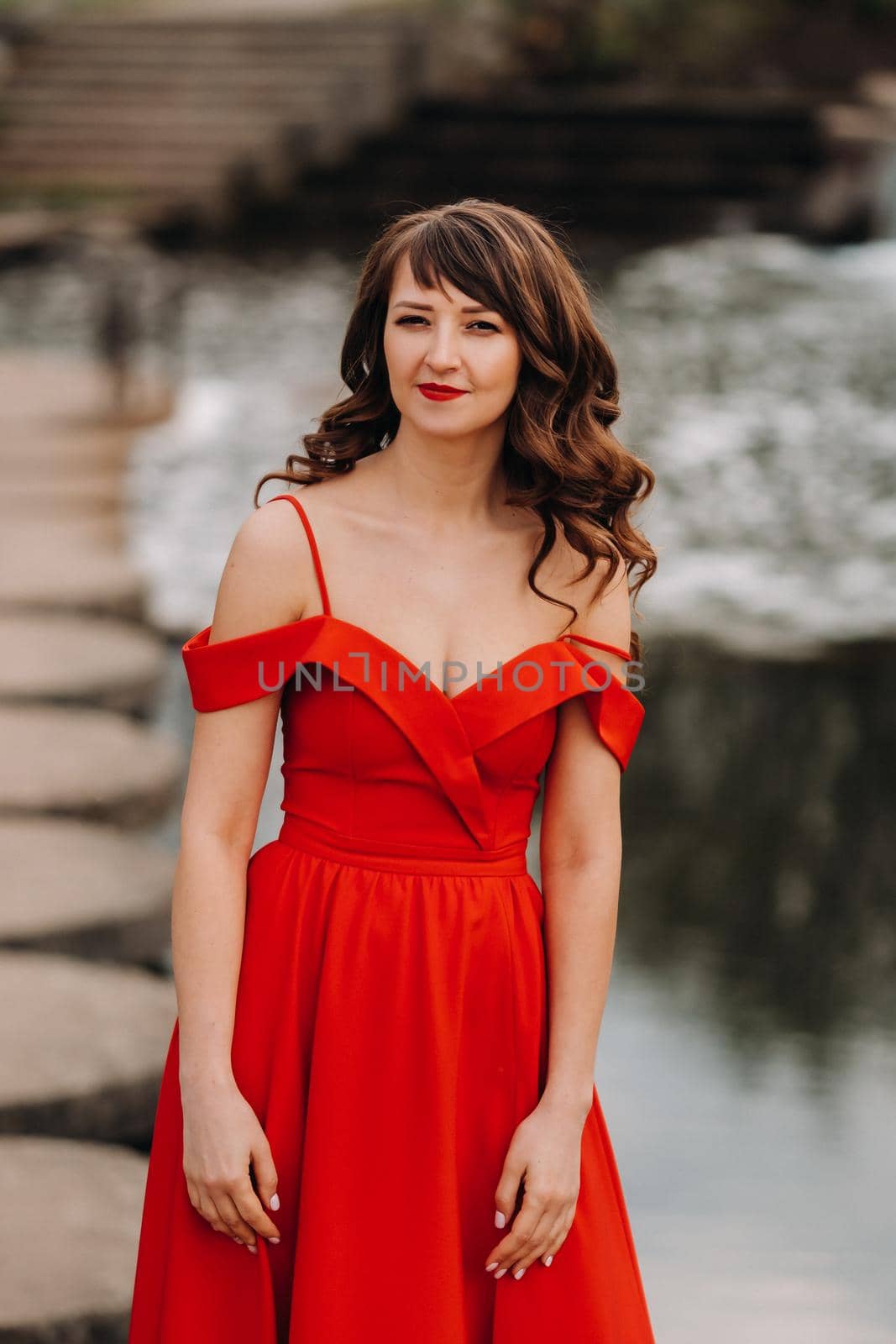 girl in a long red dress near the lake in the Park at sunset. by Lobachad