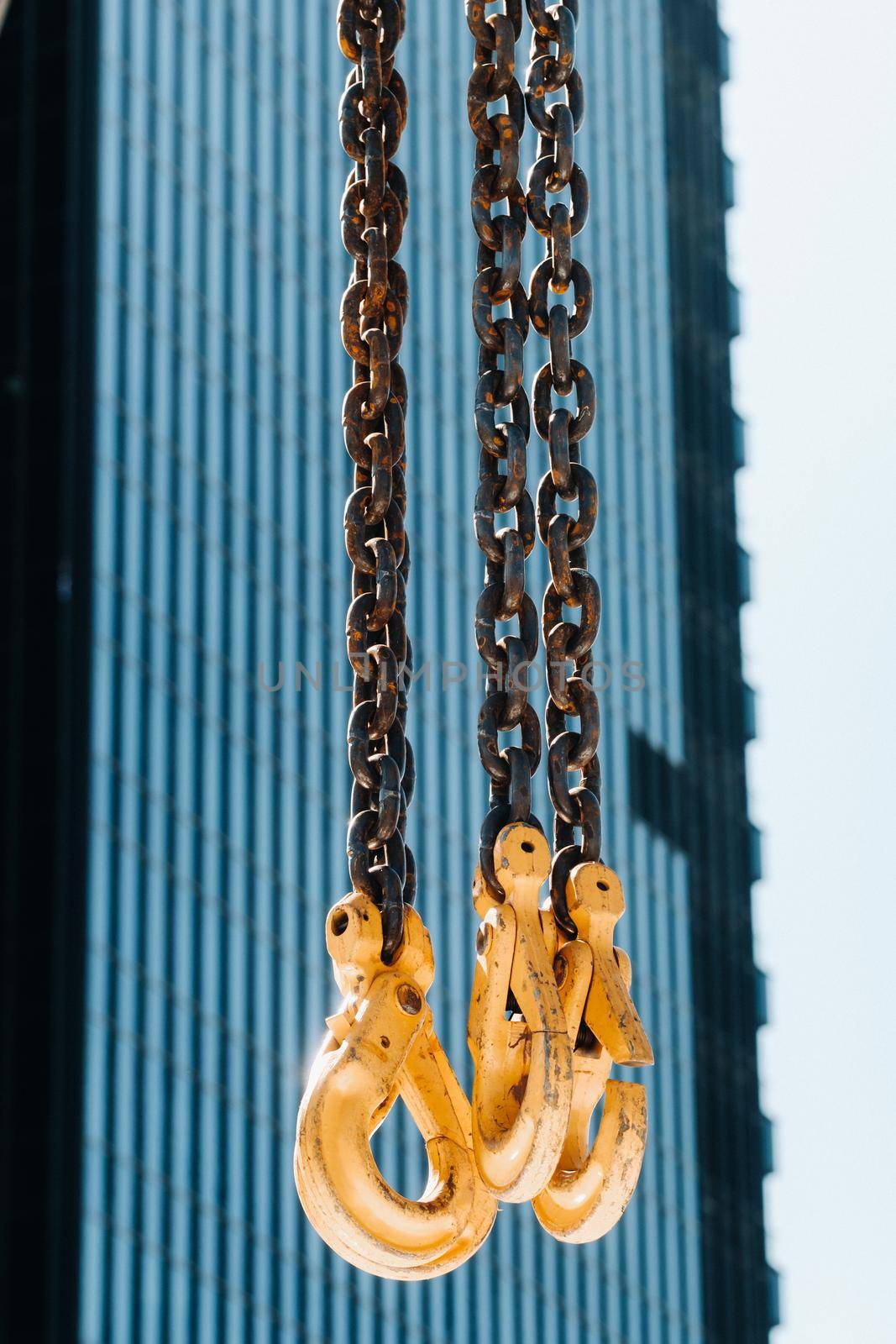 The hooks of the mobile crane near the glass of high buildings.Lots of hooks hanging from chains suspended from a crane.