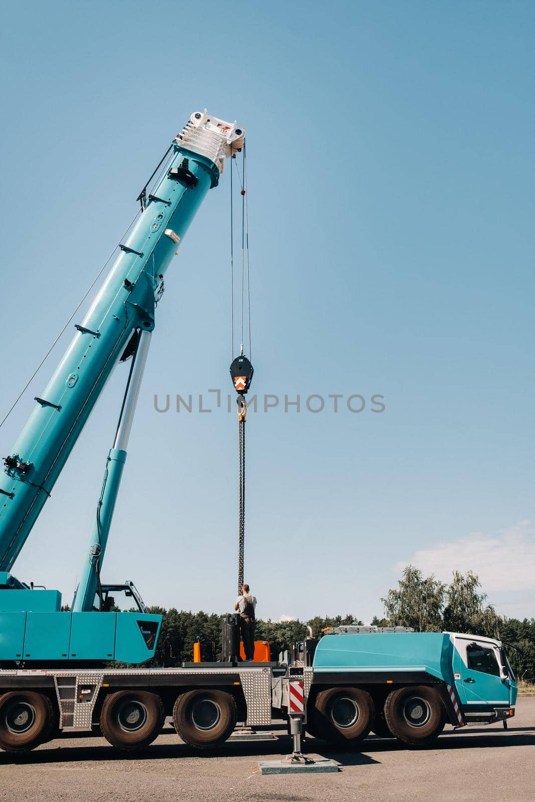 the counterweight is installed by an unrecognizable worker on a large blue car crane and is prepared to work on a site next to a large modern building. The largest truck crane for solving complex tasks. by Lobachad