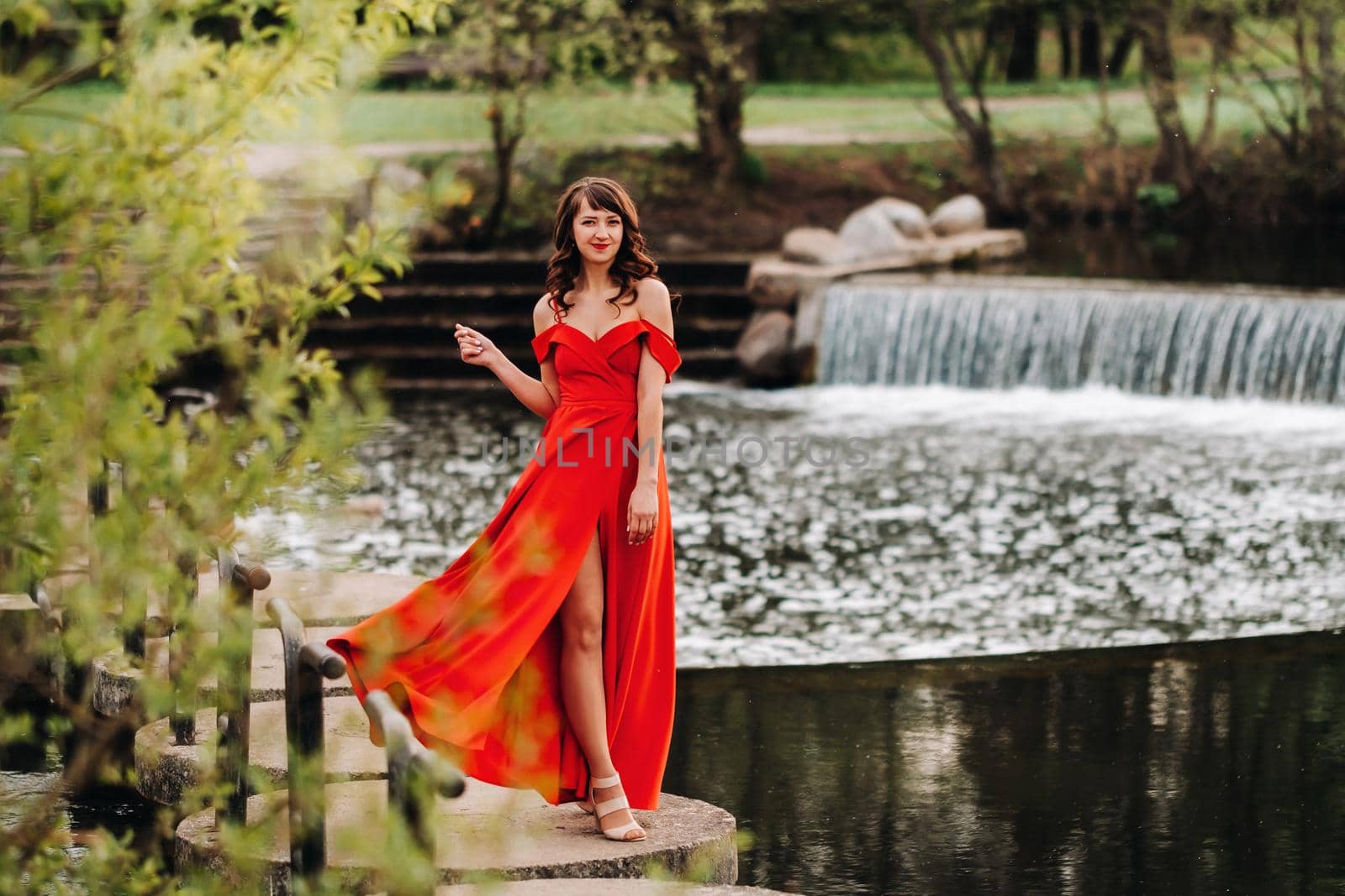 girl in a long red dress near the lake in the Park at sunset