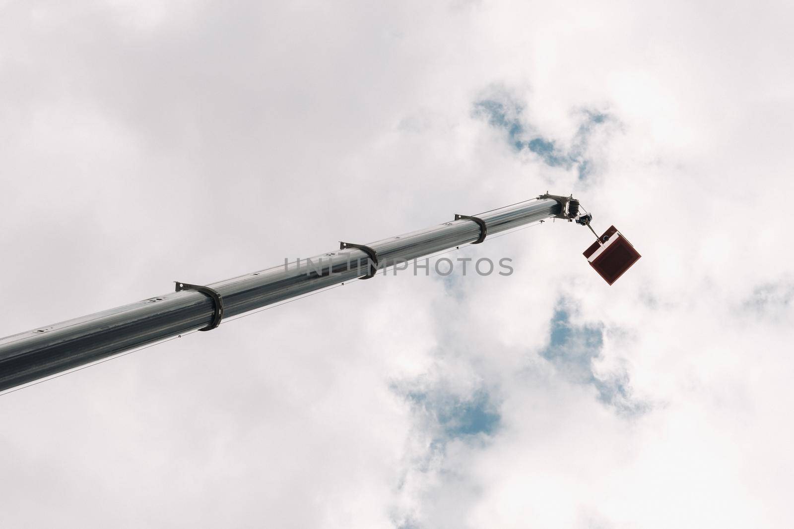 Raised high in the sky cradle of a car crane. The tallest truck crane with a yellow cradle for solving complex tasks.