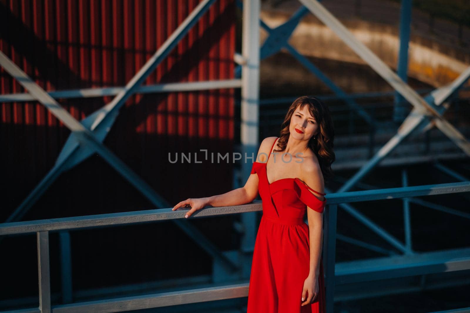 A girl in a red dress on a dam near a river at sunset.