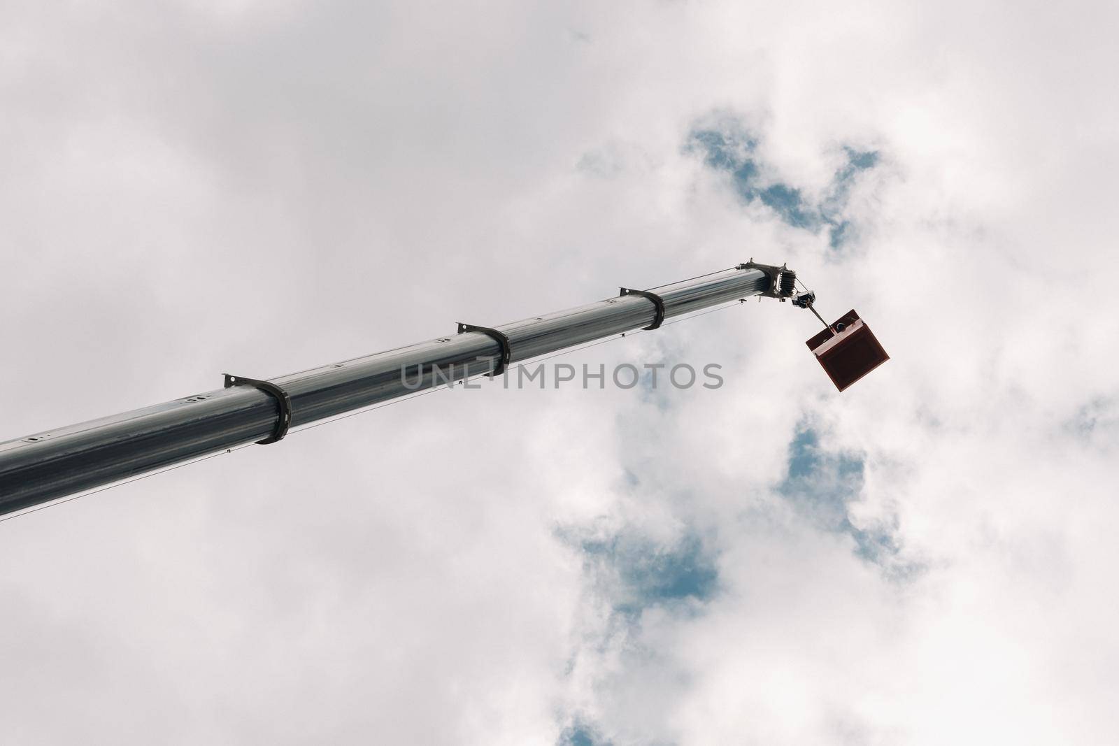 Raised high in the sky cradle of a car crane. The tallest truck crane with a yellow cradle for solving complex tasks.