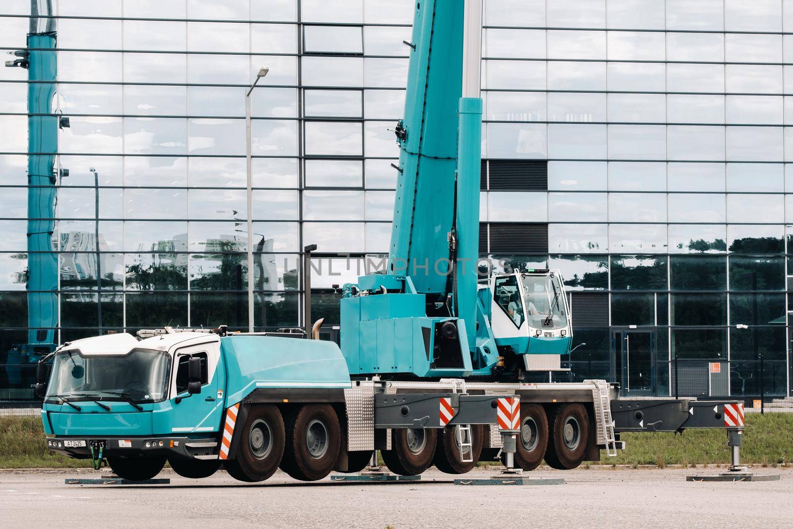 A large blue truck crane stands ready to operate on hydraulic supports on a platform next to a large modern building. The largest truck crane for solving complex tasks