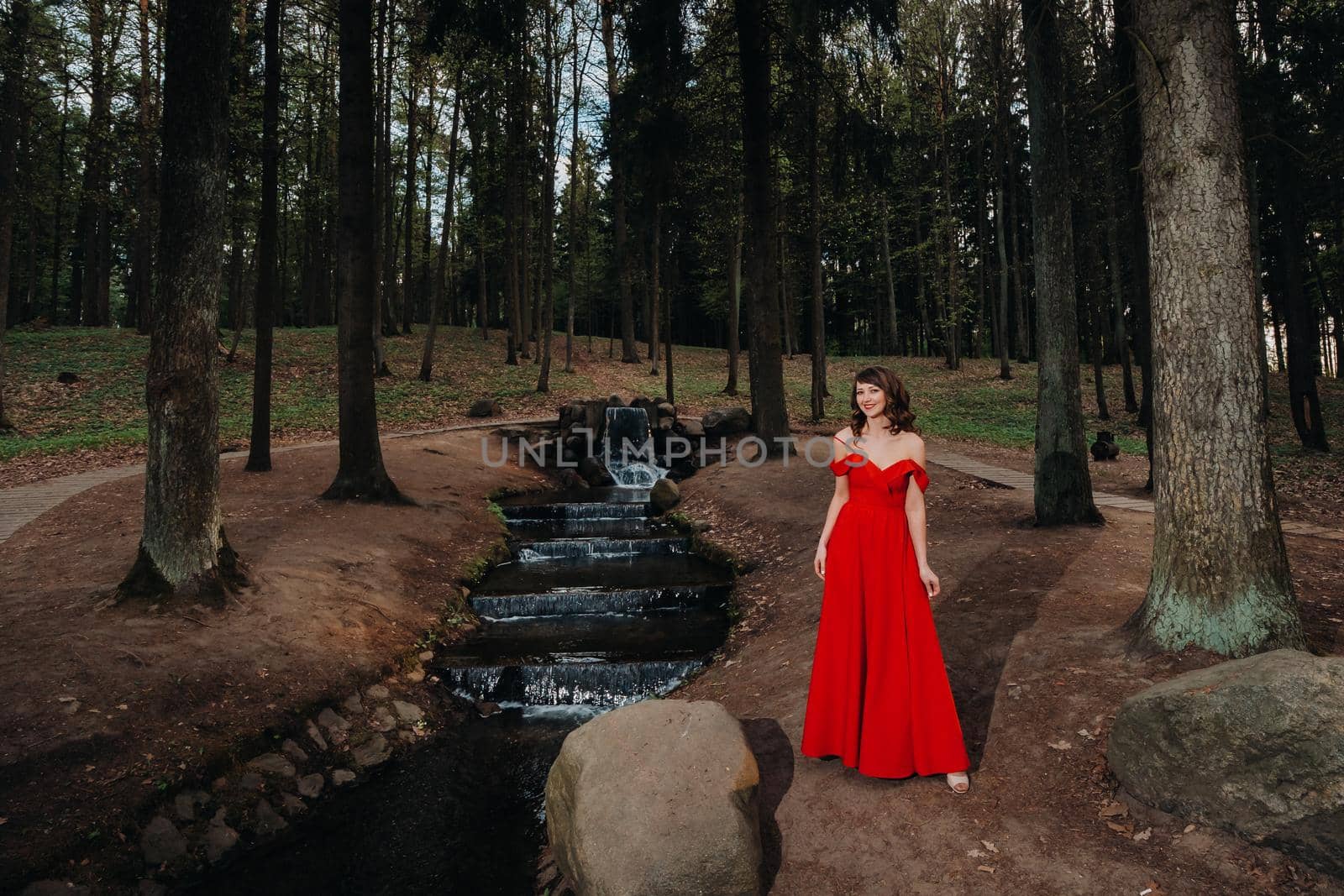 Spring Portrait of a laughing girl in a long red dress with long hair walking in the Park in the woods