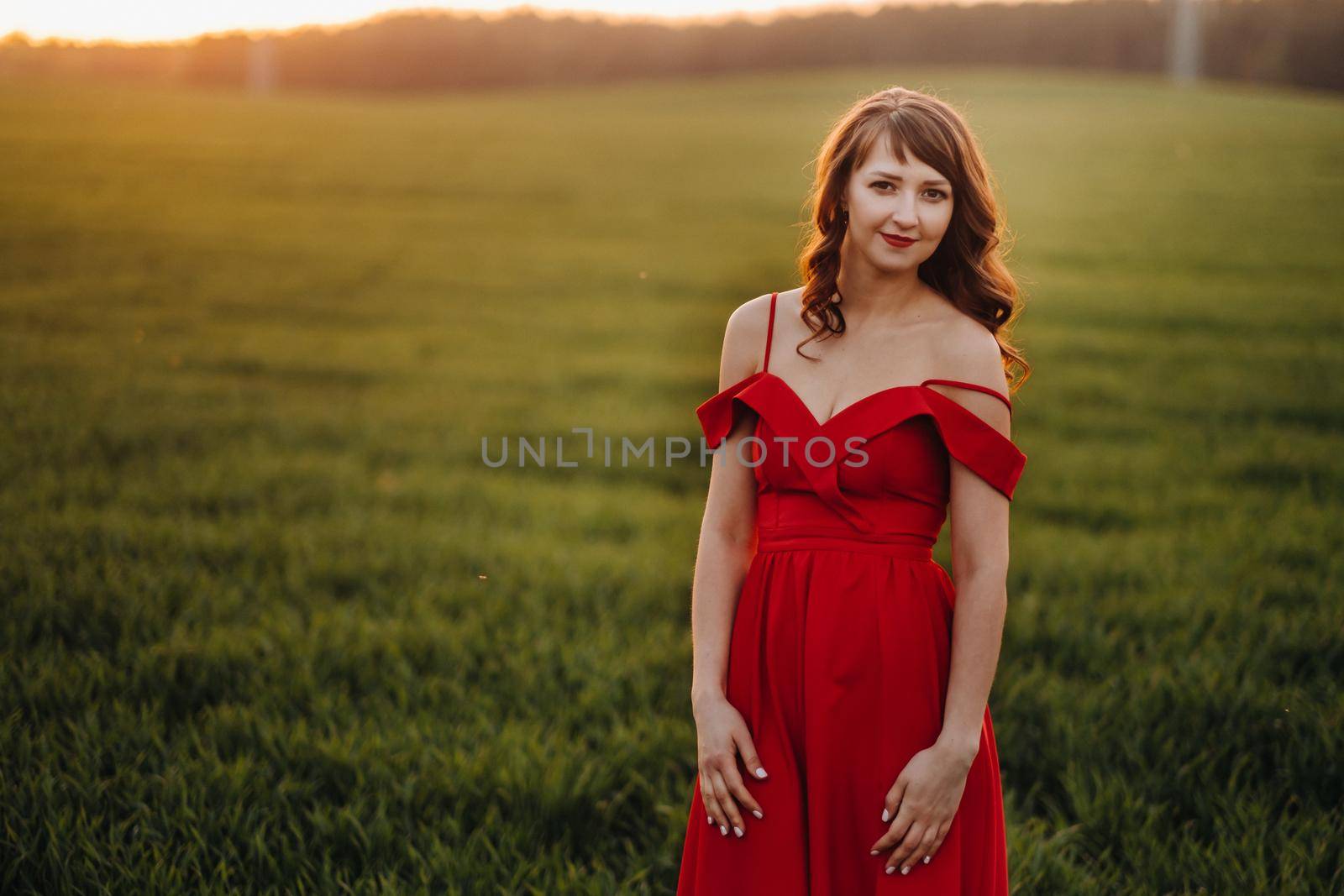 a beautiful girl in spring in a red dress is walking in a field at sunset. Taken from the air by a quadrocopter.