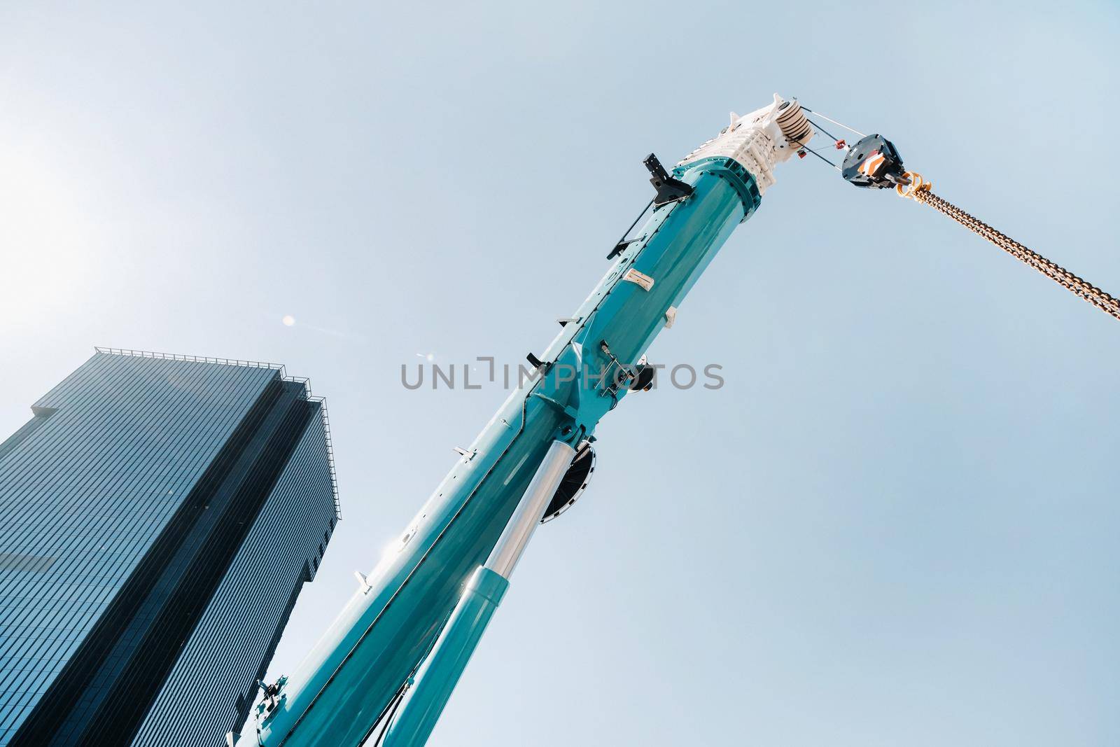 blue crane lifting mechanism with hooks near the glass modern building, crane and hydraulic high lift up to 120 meters.