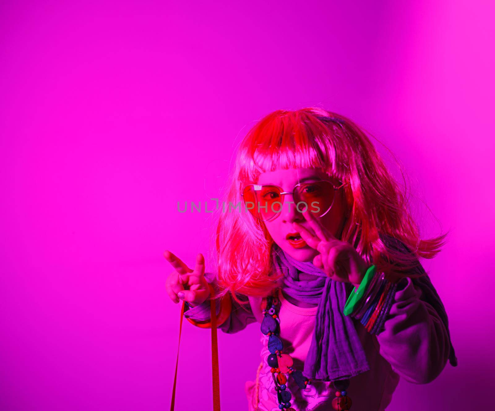 Child wearing a pink wig and heart-shaped sunglasses posed for a photo shooting on fuchsia background