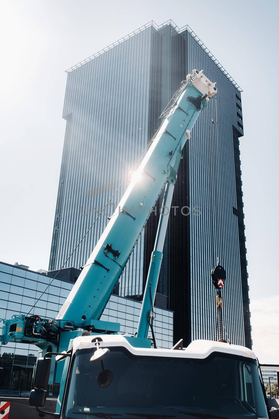 blue crane lifting mechanism with hooks near the glass modern building, crane and hydraulic high lift up to 120 meters.