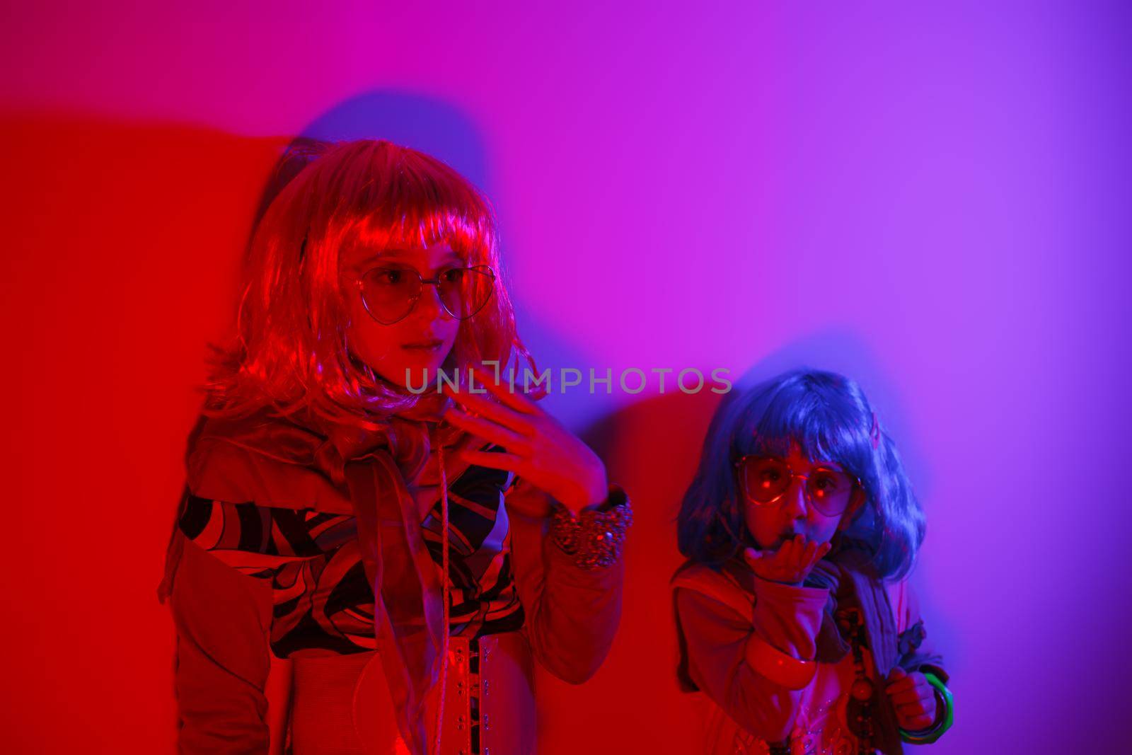 Two little girls wearing a colorful wig and heart-shaped sunglasses posed for a photo shooting on the disco light background