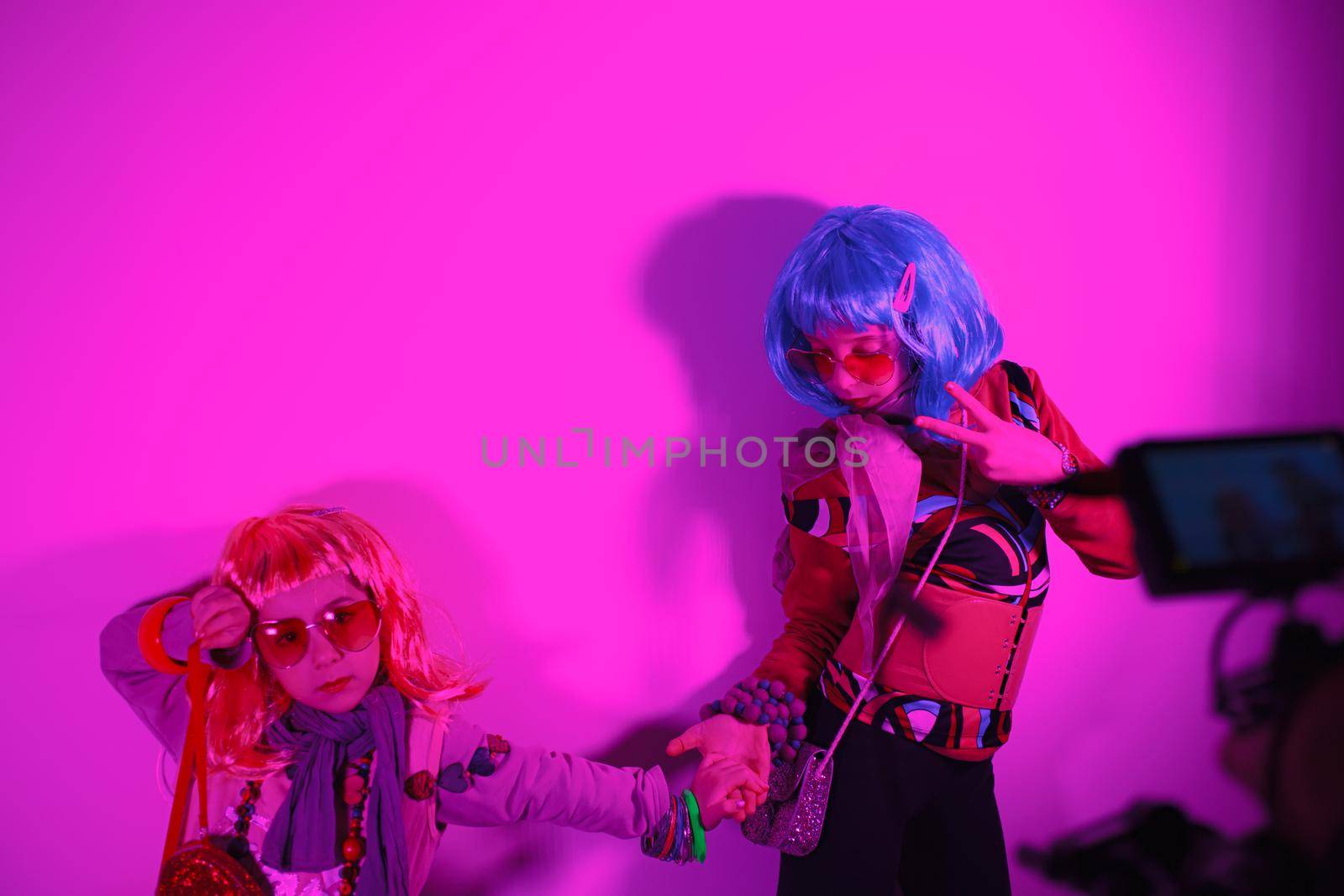 Little girls wearing a colorful wig and heart-shaped sunglasses posed for a photo shooting on the disco light background