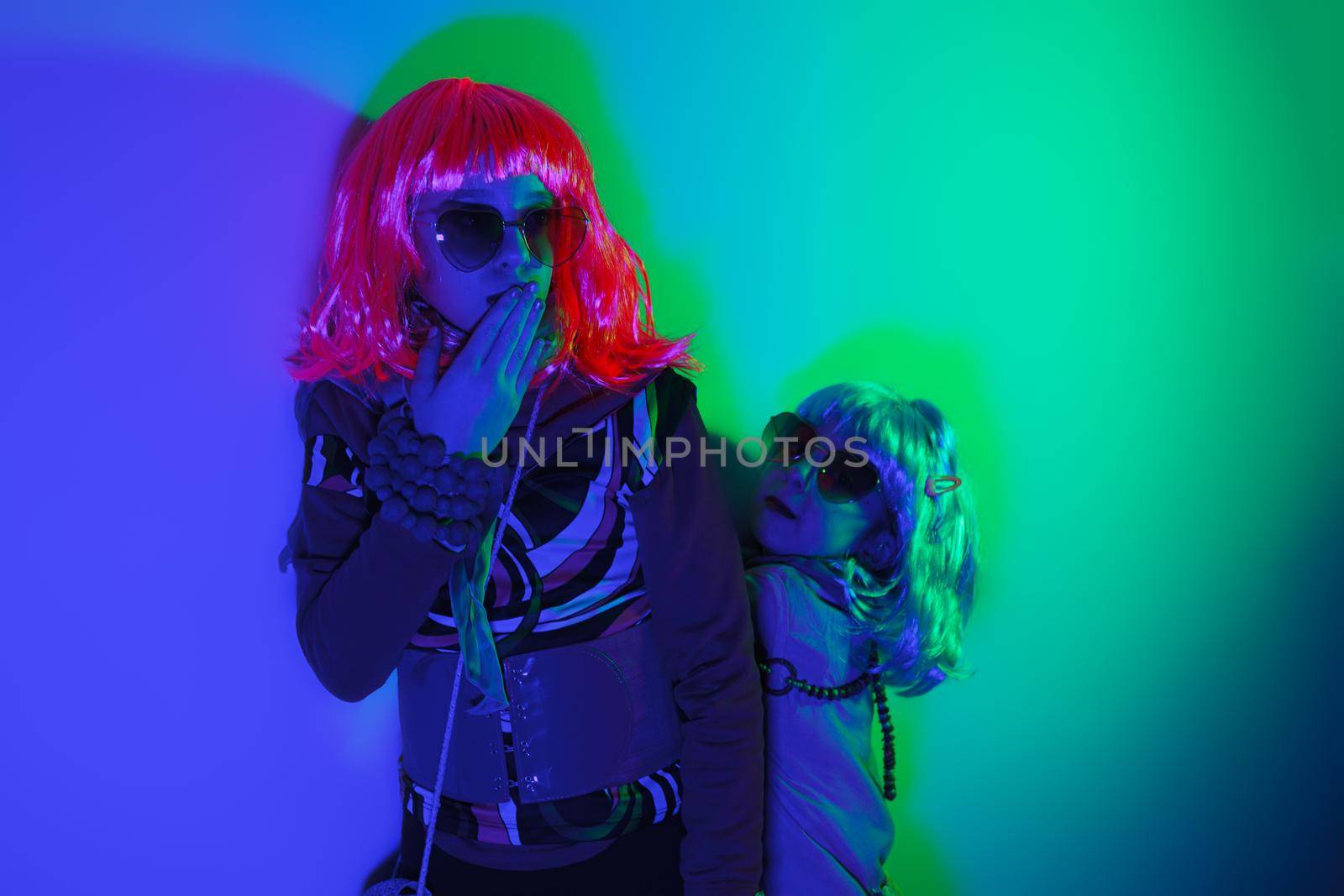 Two little girls blowing kiss wearing a colorful wig and heart-shaped sunglasses posed for a photo shooting on the disco light background