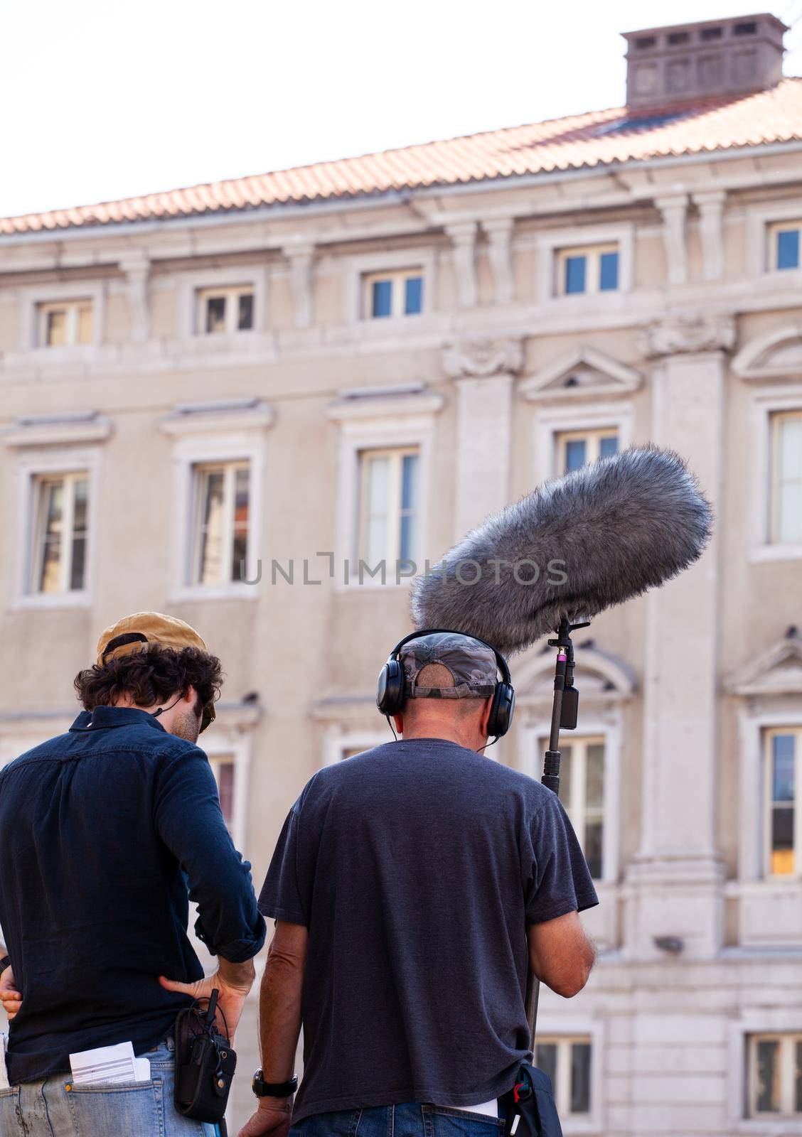 Behind the scene. Sound recorder with microphone, boom mic and headphones filming movie scene on outdoor location