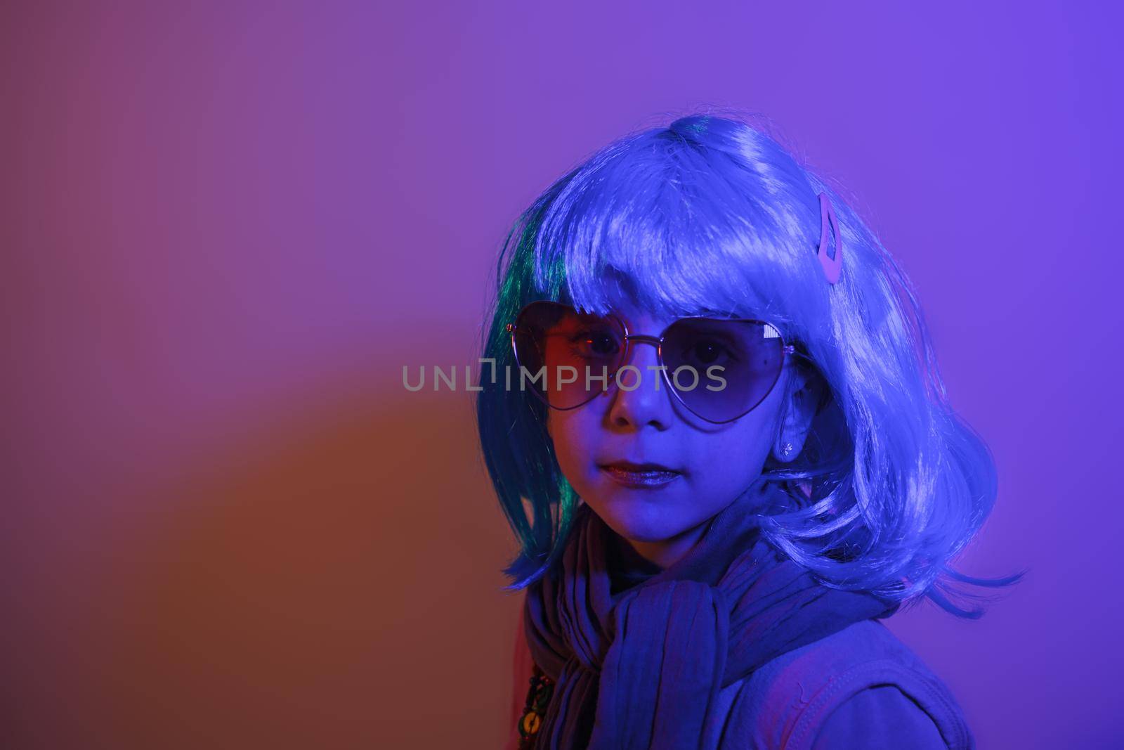 Portrait of a glamour little girl wearing colorful wig on purple background