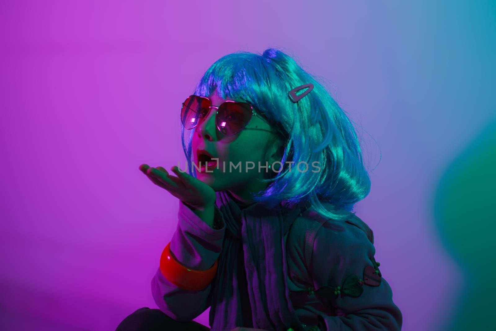 A glamour little girl posing for a photo portrait while wearing a colorful wig on pink background