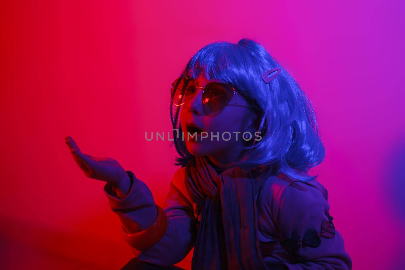 Little girl blowing kiss wearing a colorful wig and heart-shaped sunglasses posed for a photo shooting on the disco light background