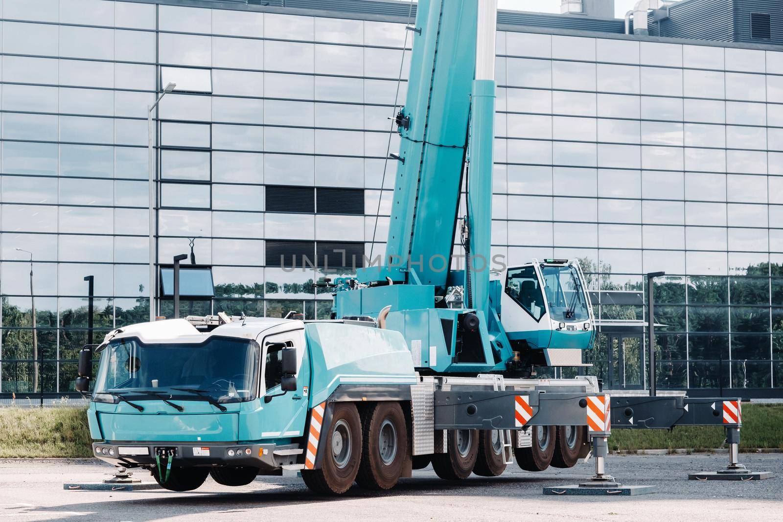 A large blue truck crane stands ready to operate on hydraulic supports on a platform next to a large modern building. The largest truck crane for solving complex tasks