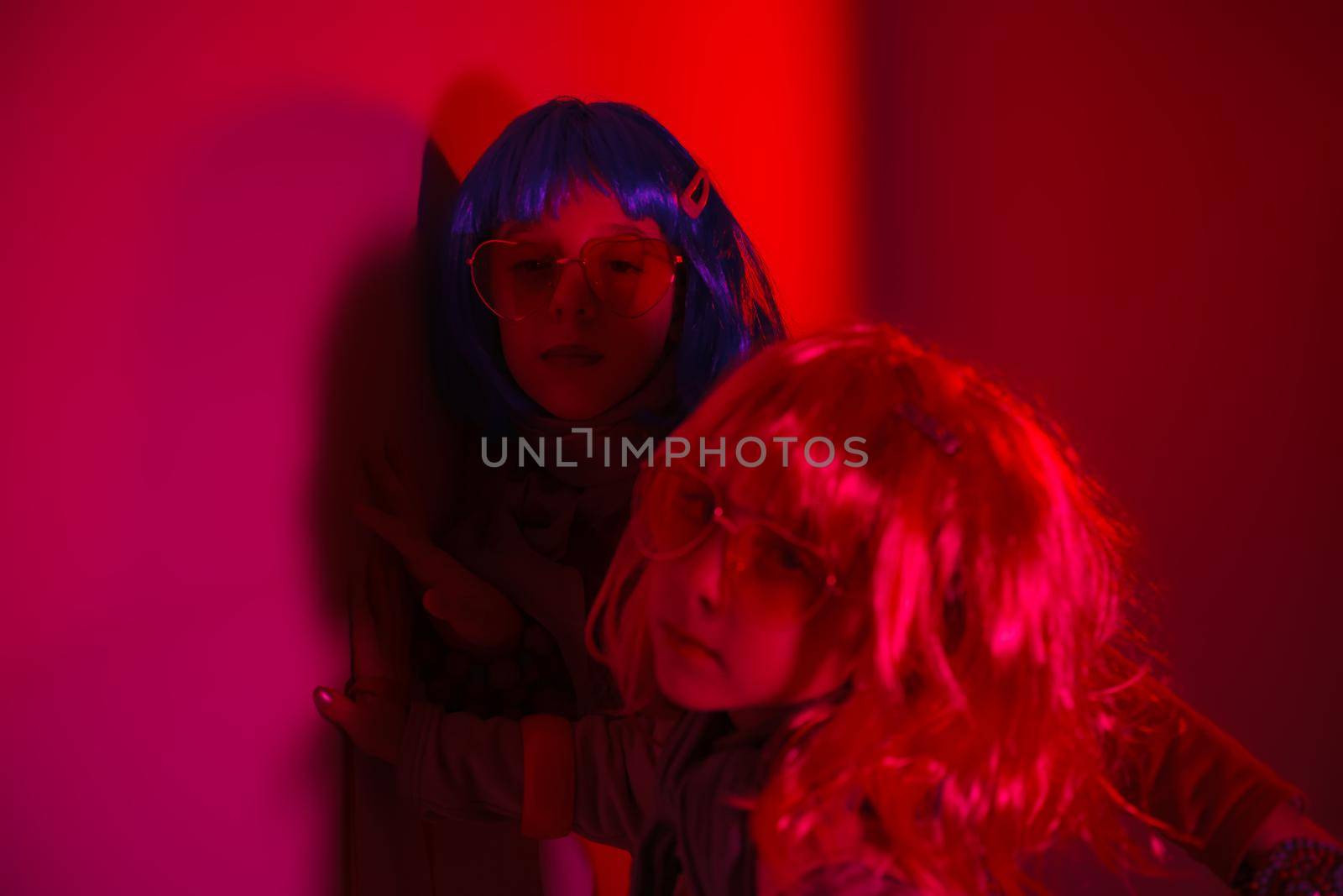 Little girls wearing a colorful wig and heart-shaped sunglasses posed for a photo shooting on the disco light background