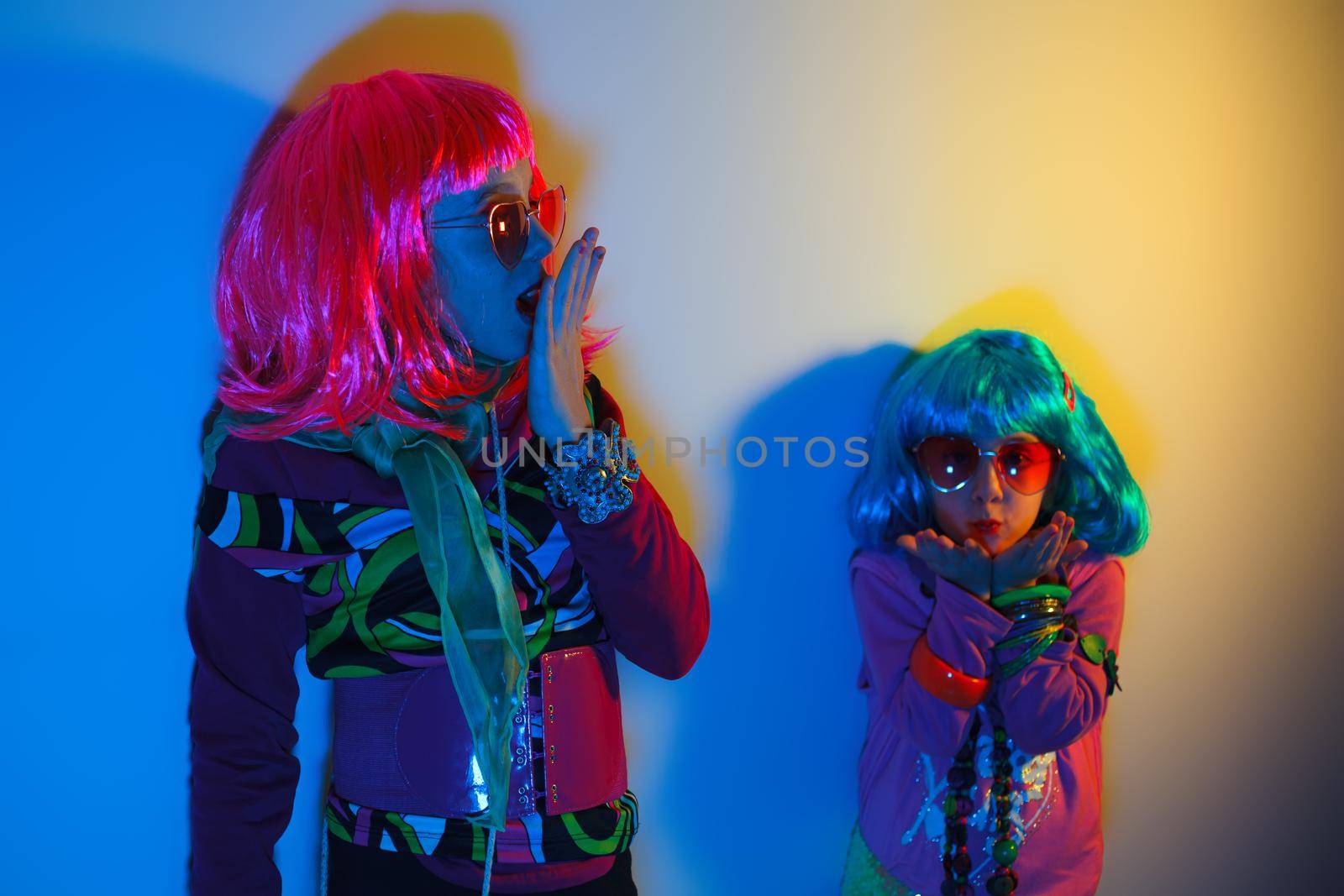 Two little girls blowing kiss wearing a colorful wig and heart-shaped sunglasses posed for a photo shooting on the disco light background