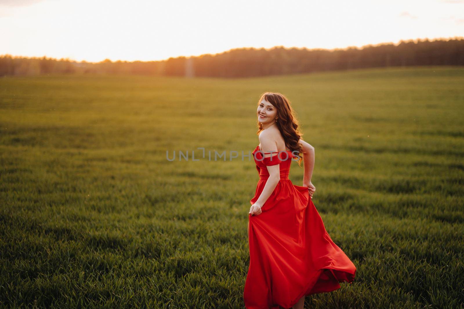 a beautiful girl in spring in a red dress is walking in a field at sunset. Taken from the air by a quadrocopter.