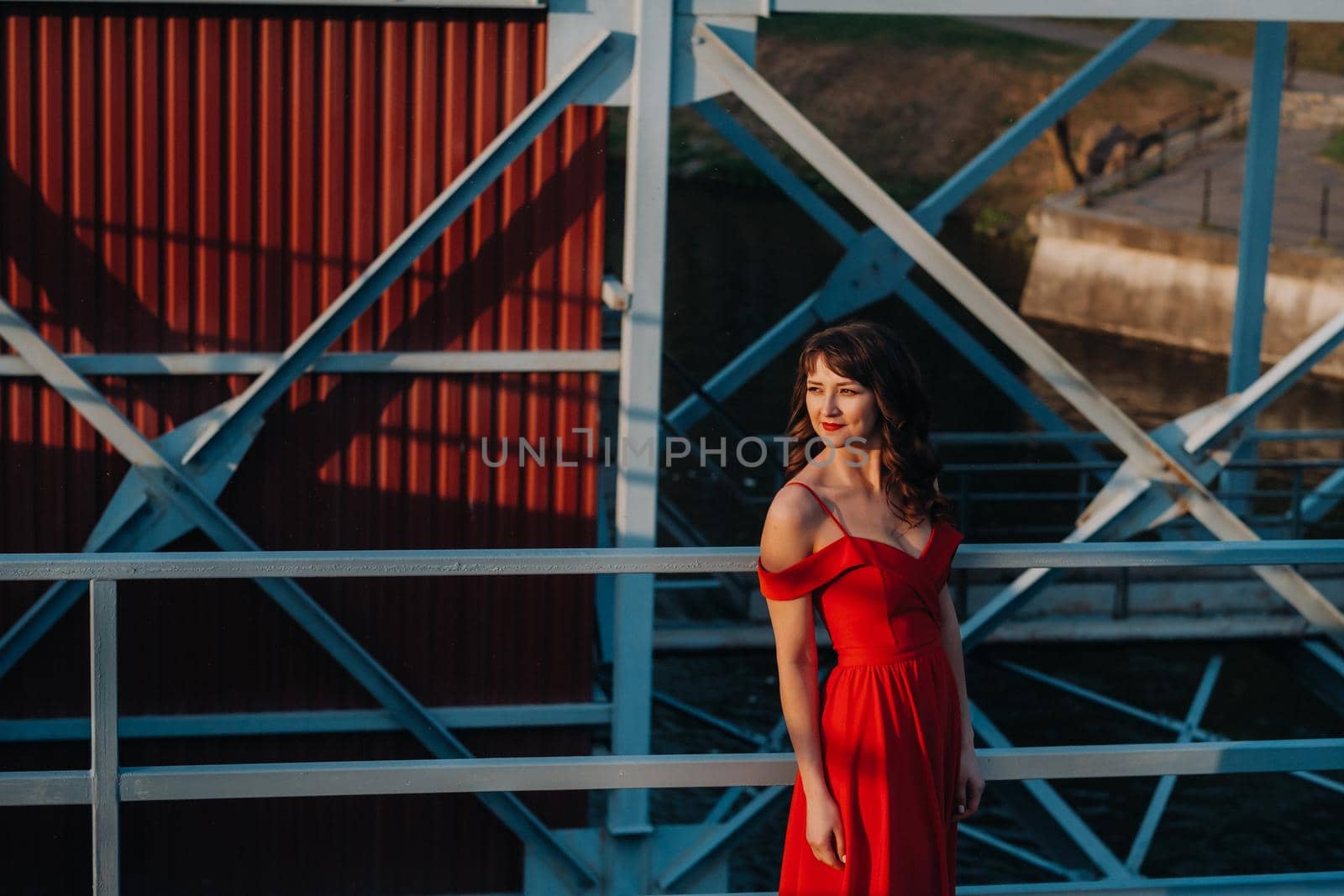 A girl in a red dress on a dam near a river at sunset.