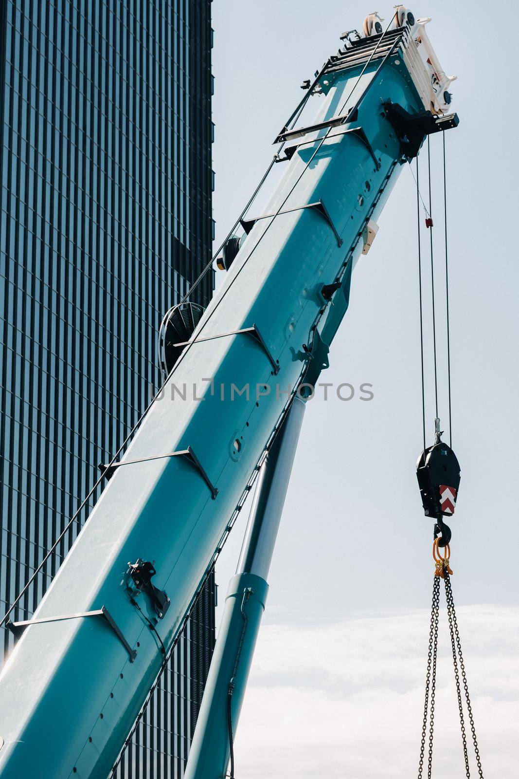 blue crane lifting mechanism with hooks near the glass modern building, crane and hydraulic high lift up to 120 meters.