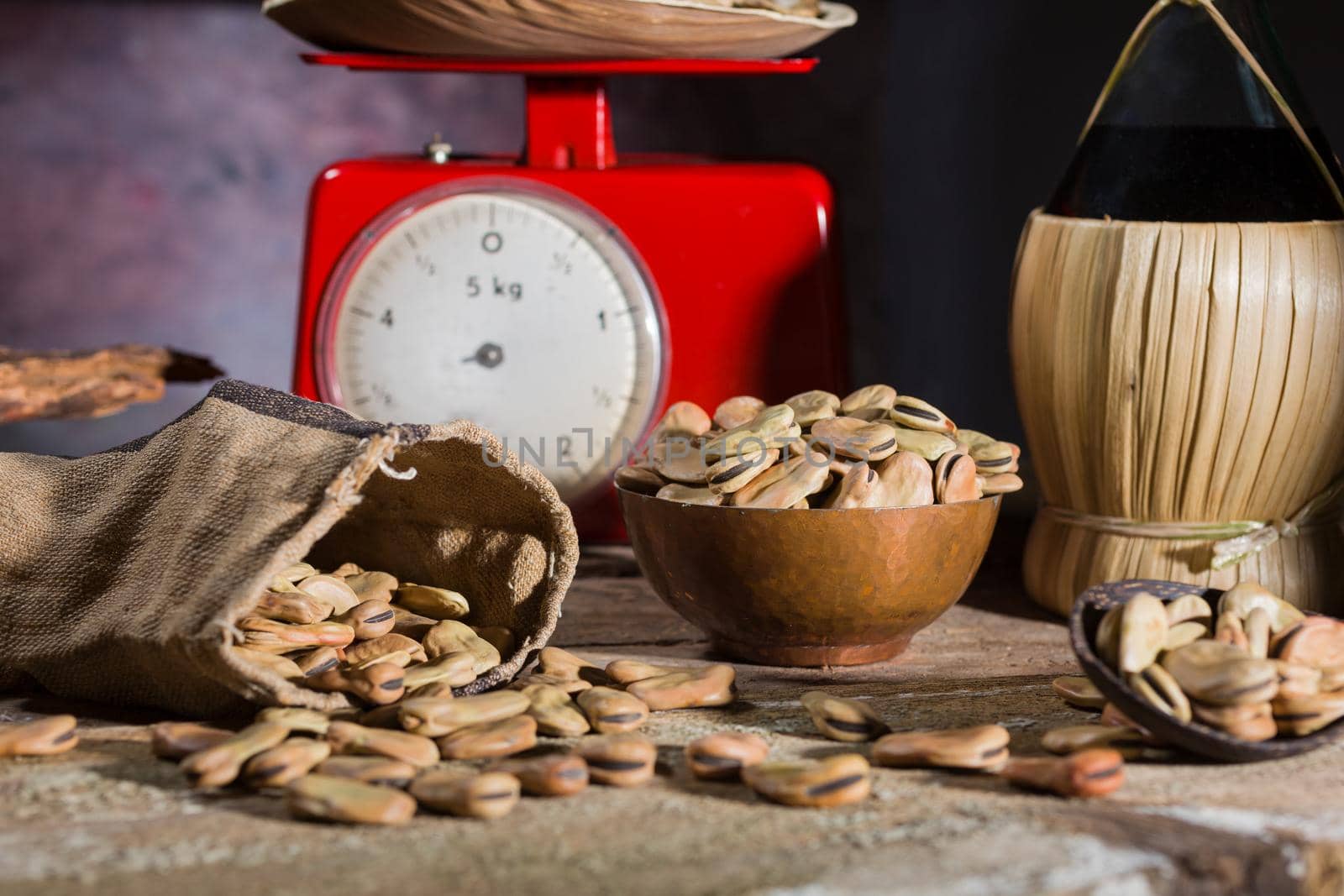 View of dried broad beans, wine and weight scale in a wooden table