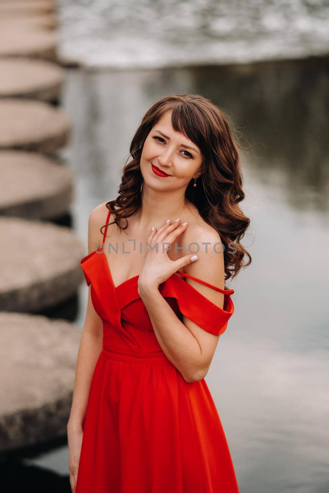 girl in a long red dress near the lake in the Park at sunset. by Lobachad