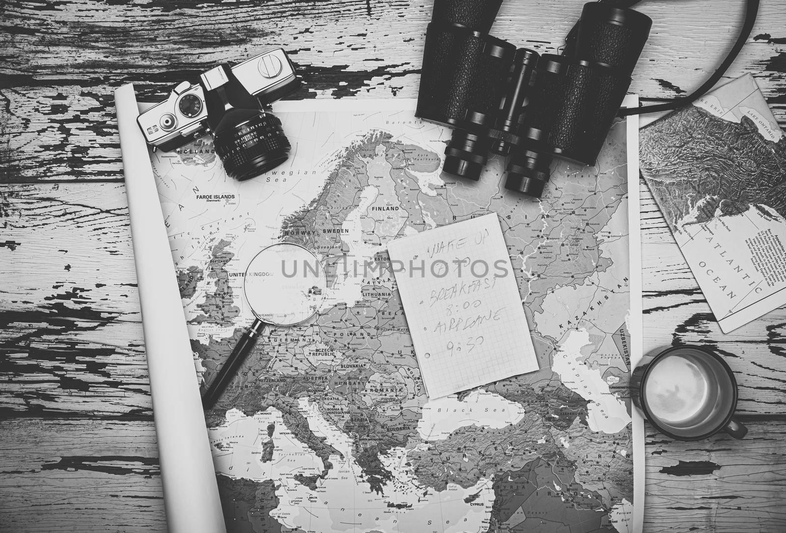 Flat lay of the travel planning concept. Top view in black and white of a note paper, binoculars, and Europe map on a wooden table