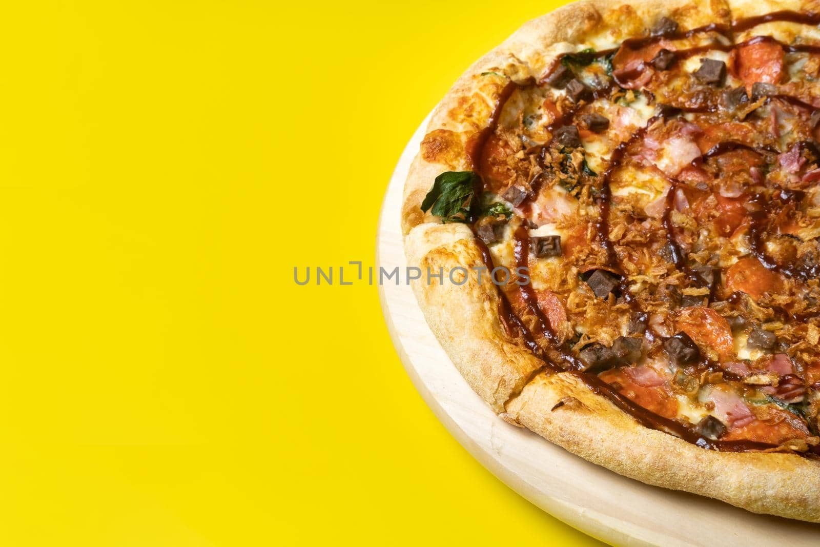 Delicious large pizza with bacon and spinach on a yellow background.