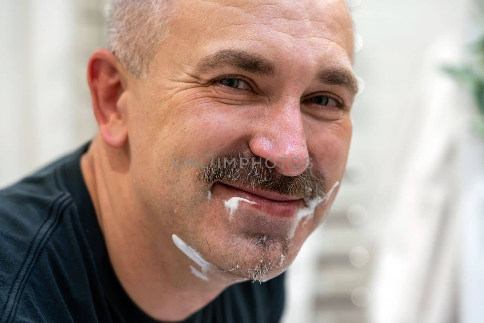Middle aged handsome man shaving his beard in bathroom by Mariakray