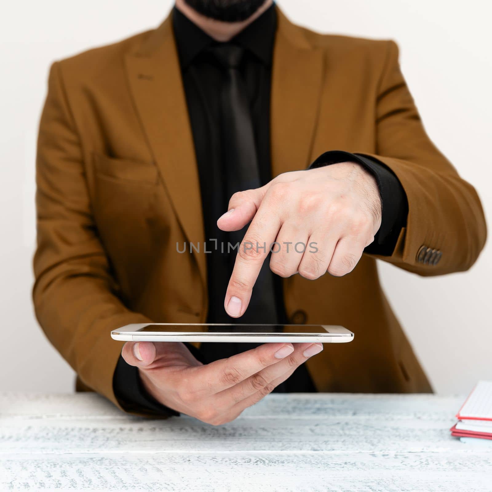 Businessman in Brown jacket sitting at table holding mobile phone And Pointing With One Finger On Important Message. Gentleman Showing Critical Announcement. by nialowwa