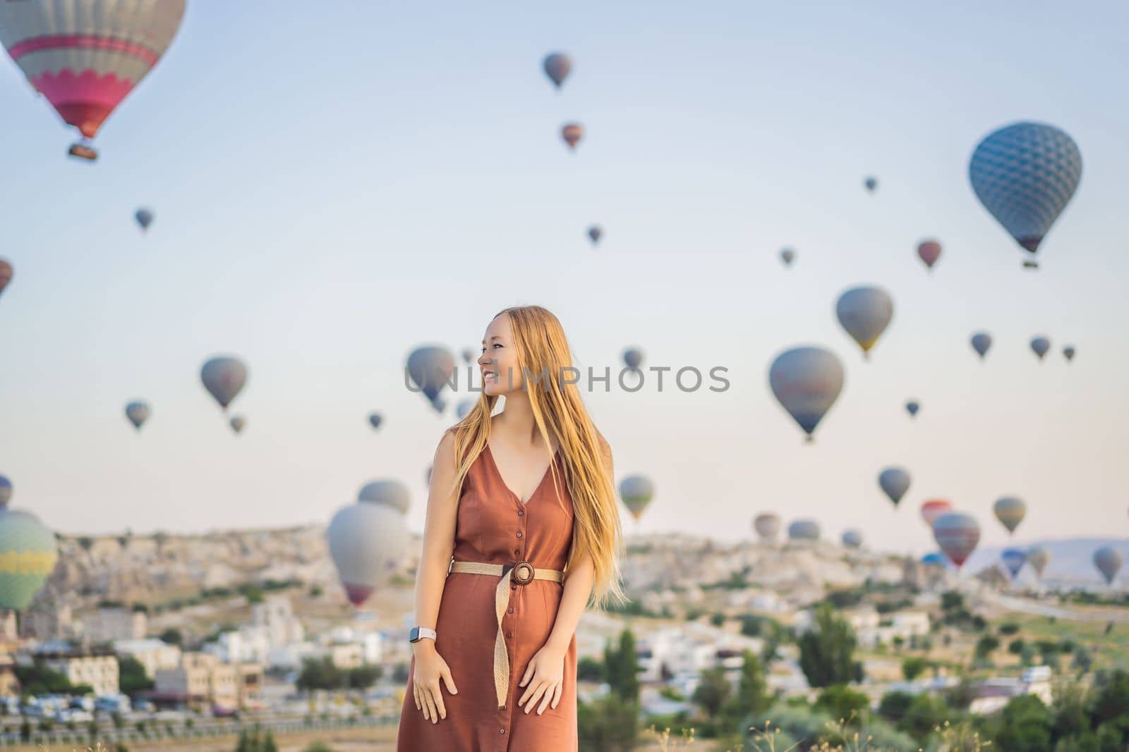 Tourist woman looking at hot air balloons in Cappadocia, Turkey. Happy Travel in Turkey concept. Woman on a mountain top enjoying wonderful view.