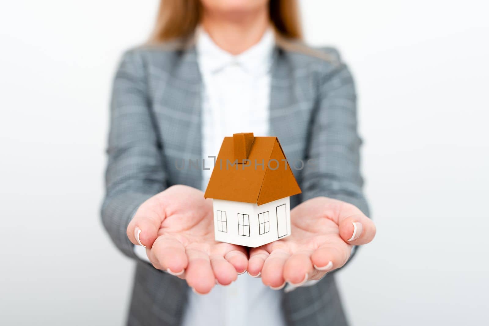 Businesswoman in a gray suit holding a colored paper house in one hand.