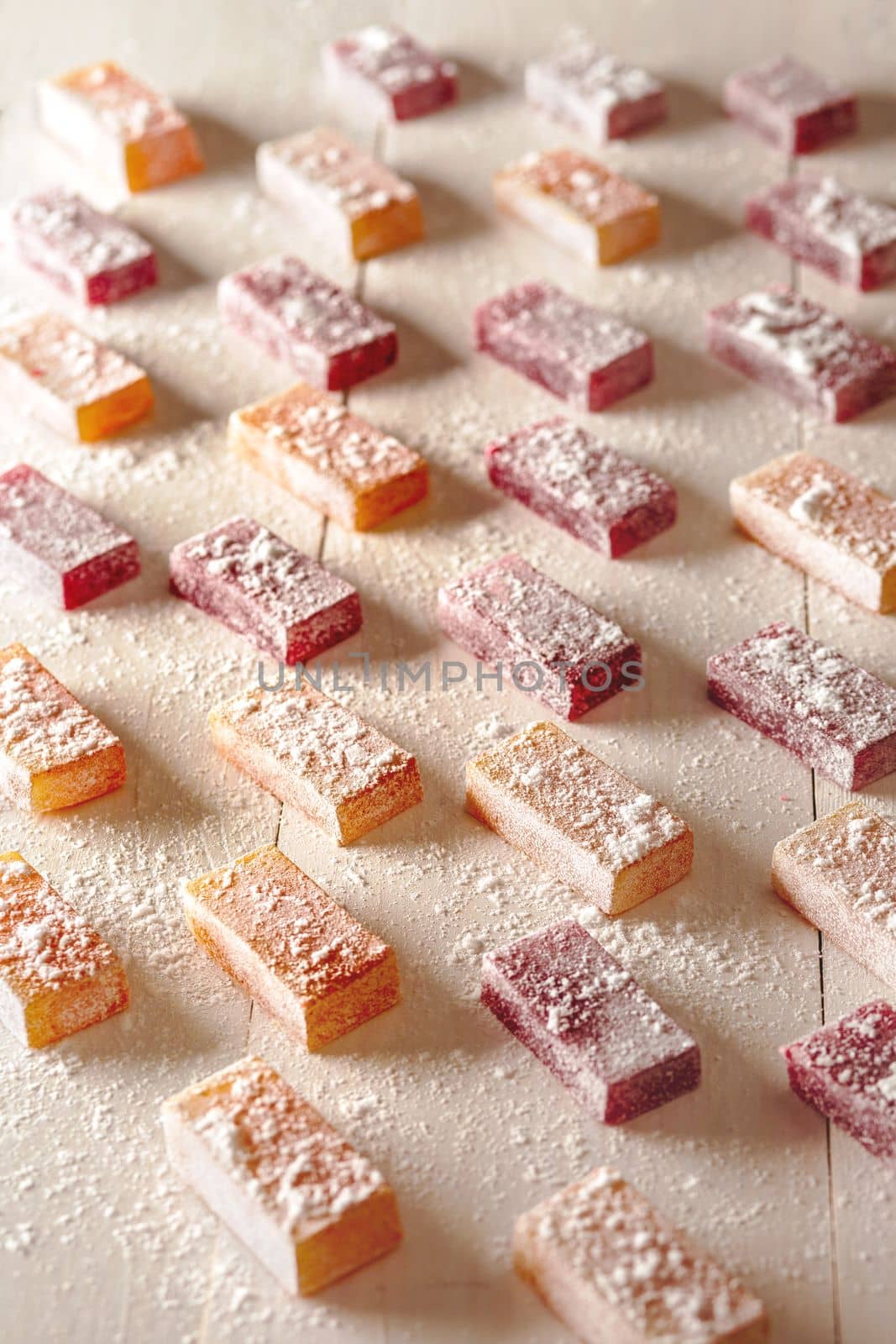 Delicious fruit and berry flavored jelly candies sprinkled with powdered sugar arranged on white wooden table. Concept of healthy natural sweets